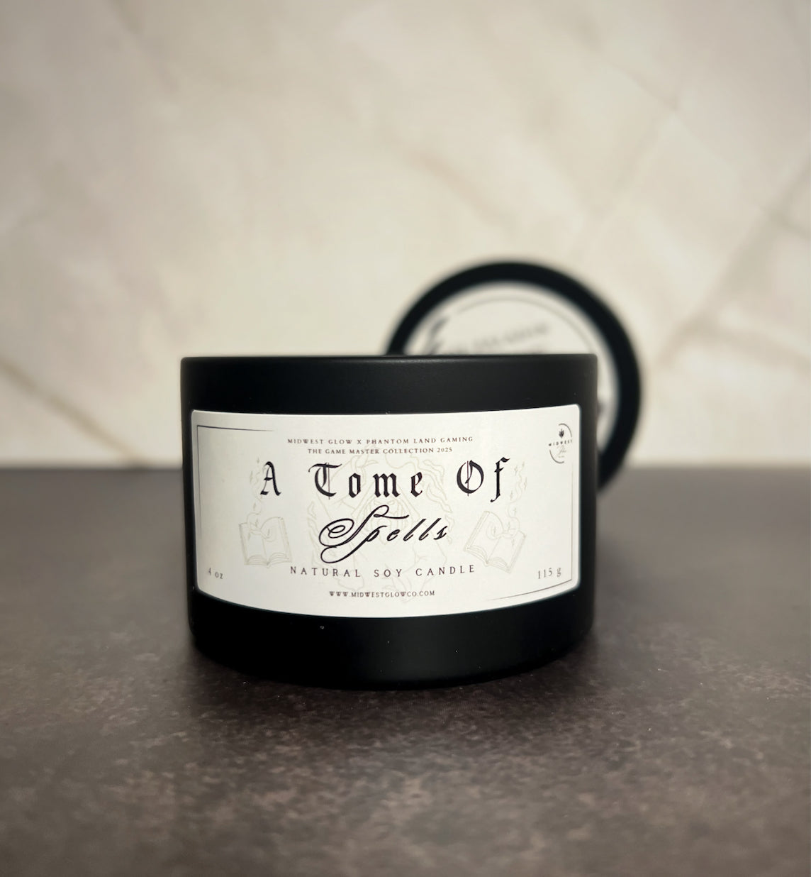 A candle in a black tin showing the label that reads A Tome Of Spells by the company Midwest Glow