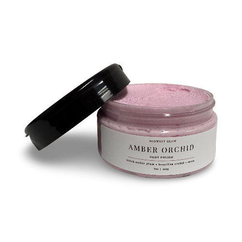 A jar of Miewest Glow Amber Orchid Roast Orchid mask, showing the light pinkish-purple textured mask inside and its black lid leaning against the jar on a white background.
