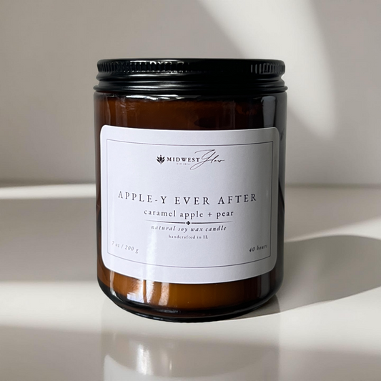 Amber glass candle jar sits on a white pristine photo blackdrop with subtle studio lighting, showcasing the Apple-Y Ever After scented soy candle by Midwest glow.