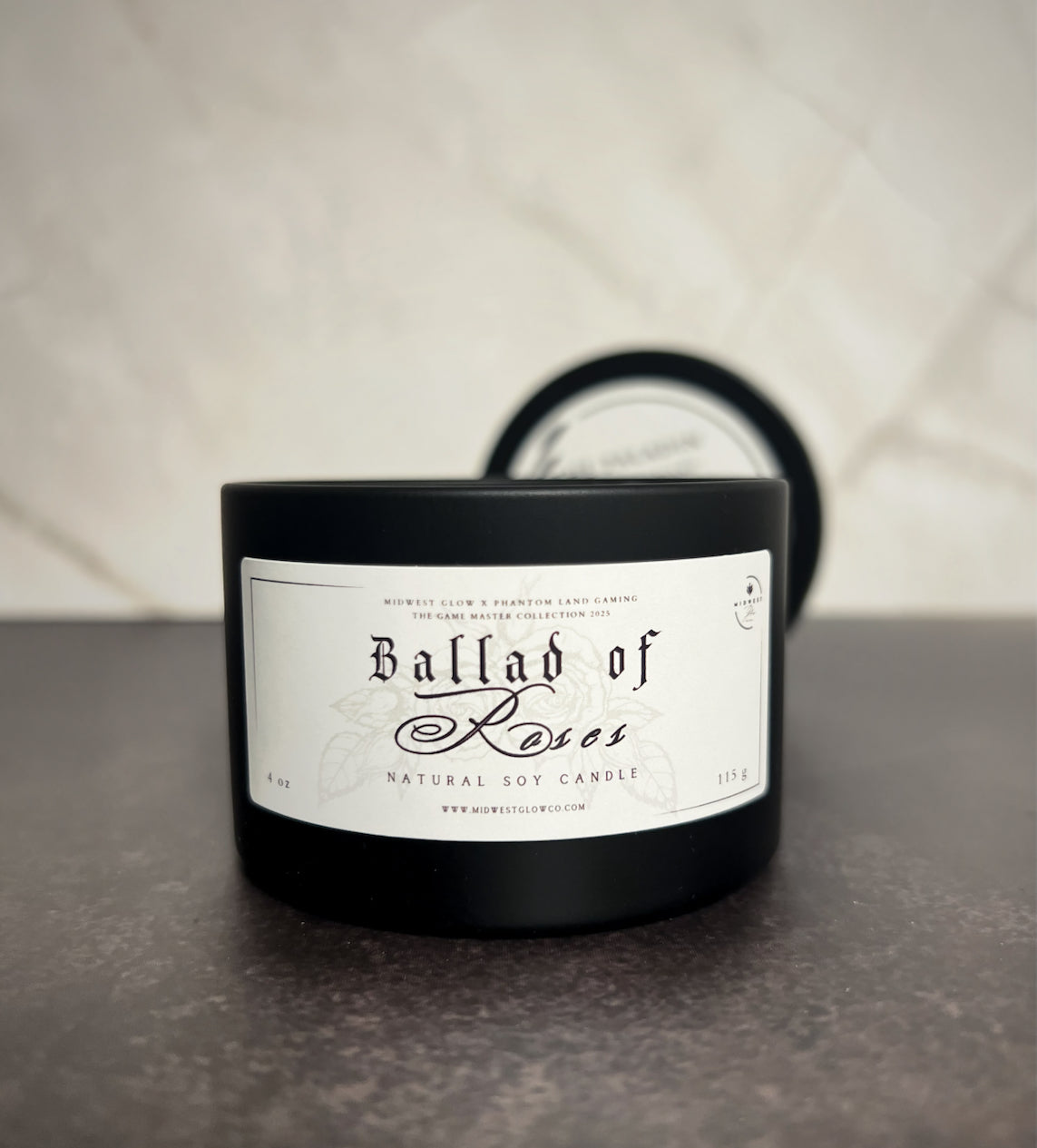 A candle in a black tin showing the label that reads Ballad Of Roses by Midwest Glow