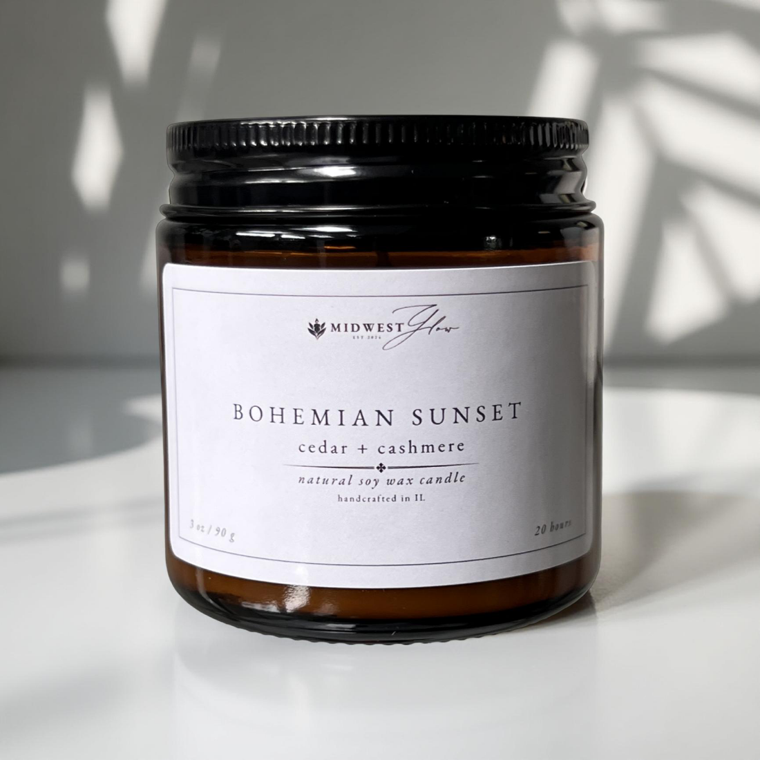 A smaller 3 oz version of the popular Bohemian Sunset candle by Midwest Glow is sitting against a white wall photo backdrop with natural lighting and shadows