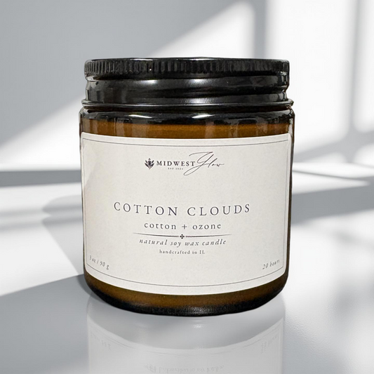 Candle jar labeled 'Cotton Clouds' with a black lid on a reflective surface.