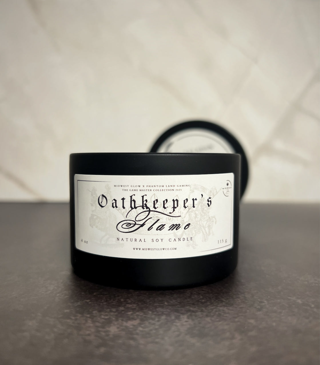 A candle in a black tin showing the label that reads Oathkeeper's Flame by the company Midwest Glow.