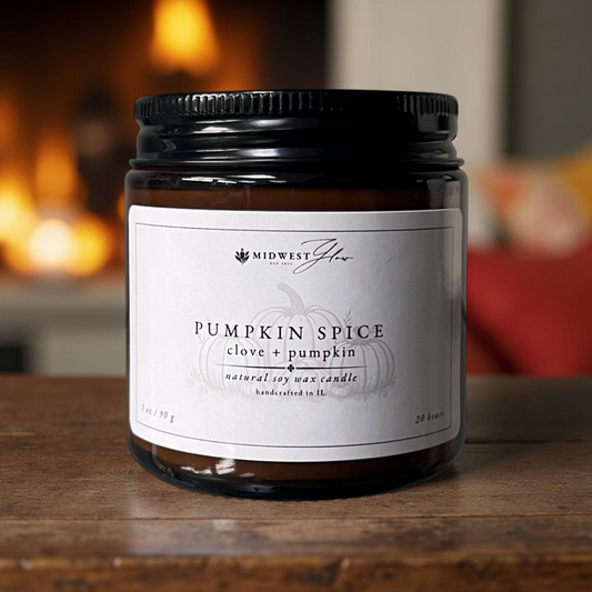 Pumpkin spice candle in a jar with a label on a wooden surface, fireplace in the background