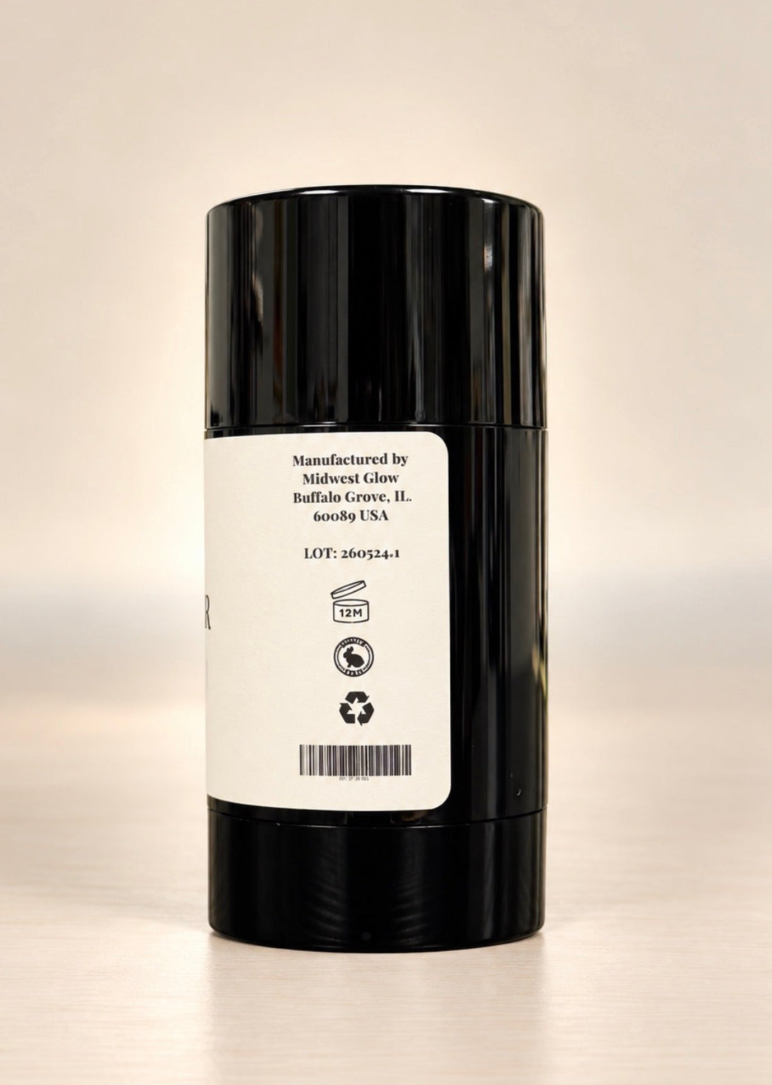 A black cylindrical cosmetic stick container with a white label on a light beige background.