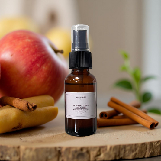 Bottle of spiced cider spray with apples and cinnamon sticks on a wooden surface