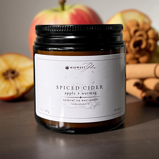 Spiced cider candle with apples and cinnamon sticks in the background