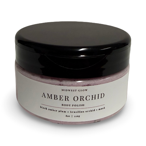 Midwest Glow Amber Orchid body polish in a clear jar with a black lid and a white label, shown on a white background.