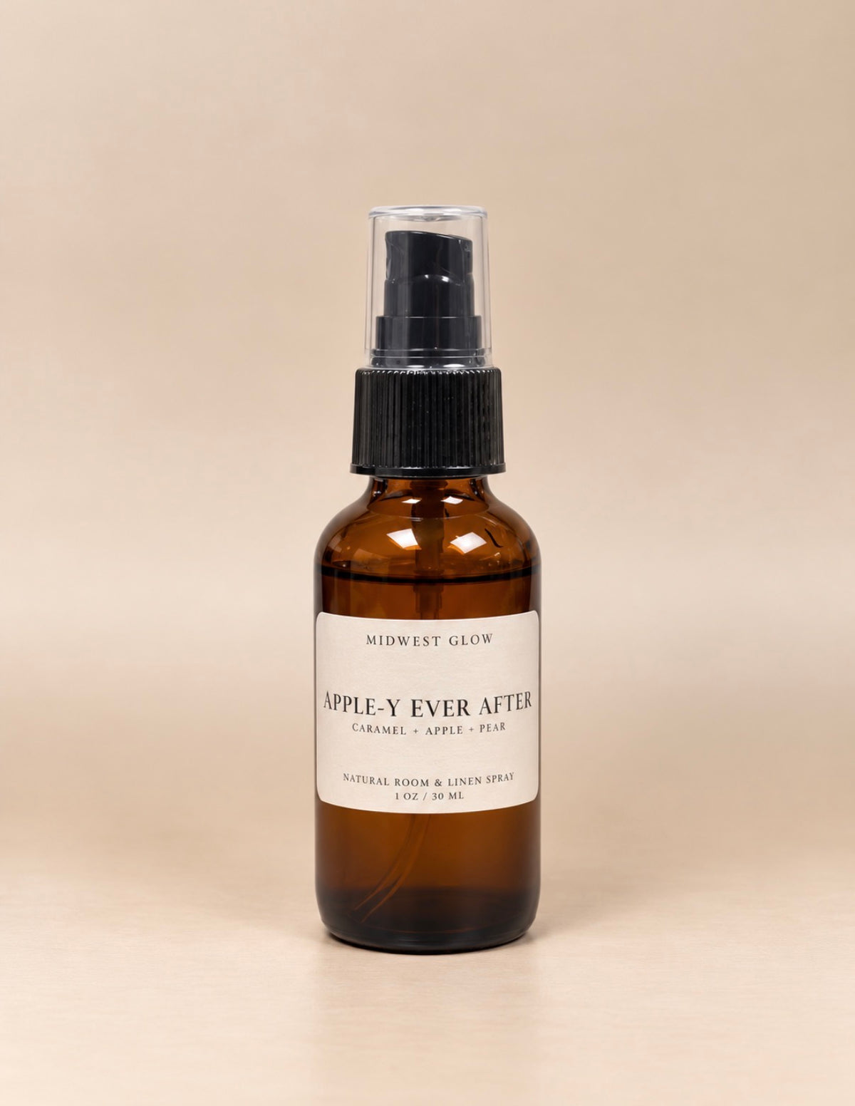 Midwest Glow Apple-Y Ever After natural room and linen spray in an amber glass bottle with a black spray pump and a cream label, set against a solid beige background.
