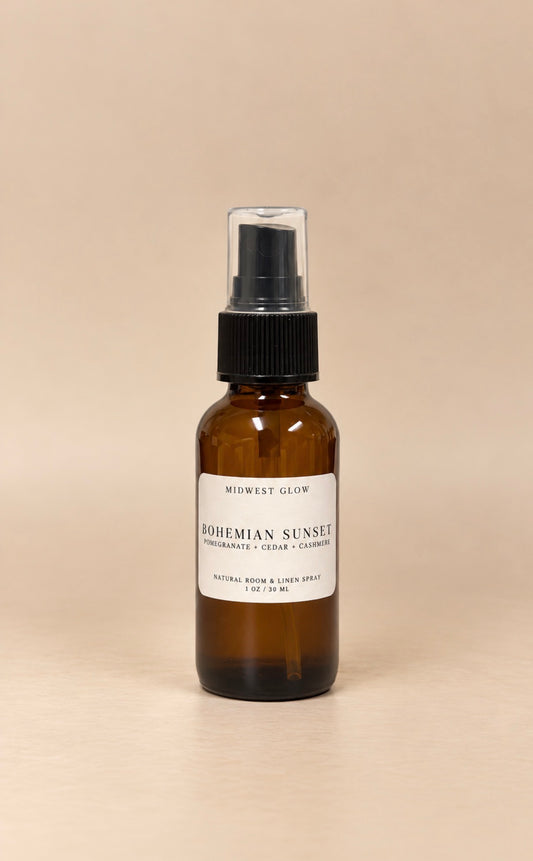 An amber glass room spray bottle with a black spray cap and a white label reading 'Midwest Glow Bohemian Sunset', set against a solid beige background.