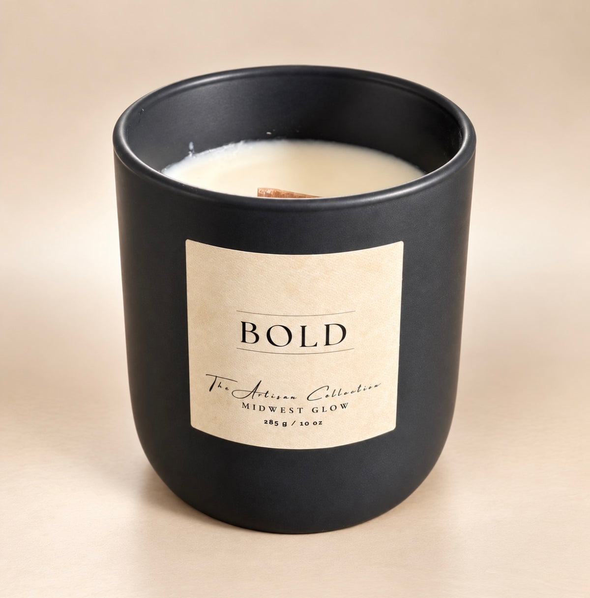 A matte black glass jar candle with a cream-colored wax and a beige label that reads 'BOLD' and 'The Artisan Collective MIDWEST GLOW'.