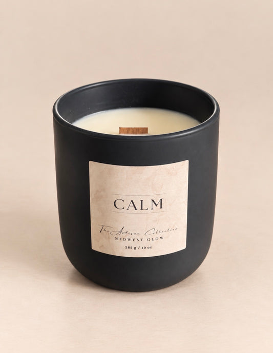 A matte black glass jar candle with a cream-colored wax and a beige paper label that reads 'CALM' and 'The Aromas Collection'.