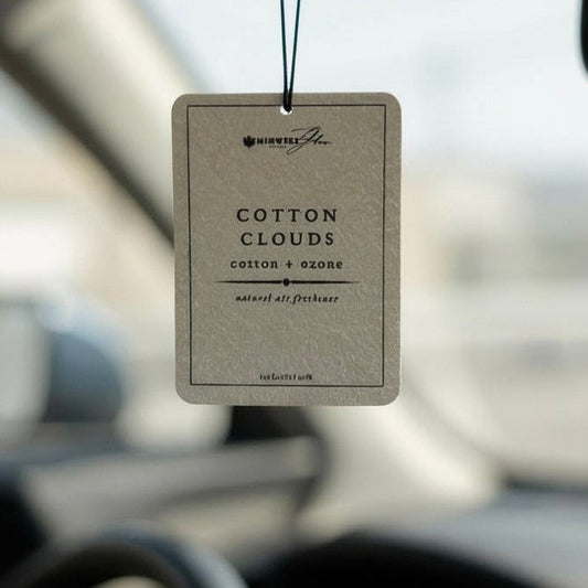 Car air freshener hanging from a car's rearview mirror with a blurred background.