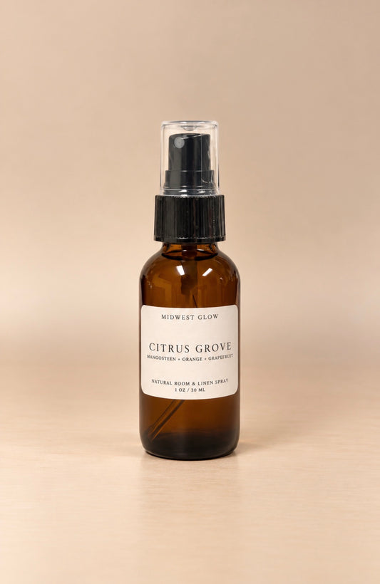 An amber glass spray bottle with a black pump and clear cap, featuring a white label that reads 'MIDWEST GLOW CITRUS GROVE', set against a solid beige background.