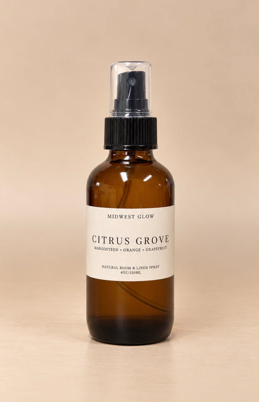 An amber glass spray bottle with a black pump and a white label reading 'MIDWEST GLOW CITRUS GROVE', set against a solid beige background.