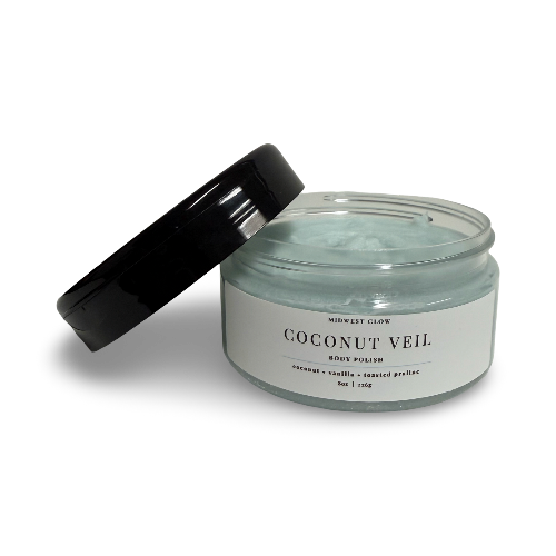 An open jar of Midnight Glow Coconut Veil Body Polish with its black lid leaning against it, set against a plain white background.