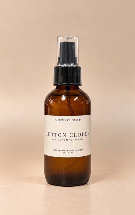 An amber glass spray bottle with a black pump and a white label reading 'MIDWEST GLOW COTTON CLOUDS', set against a solid beige background.