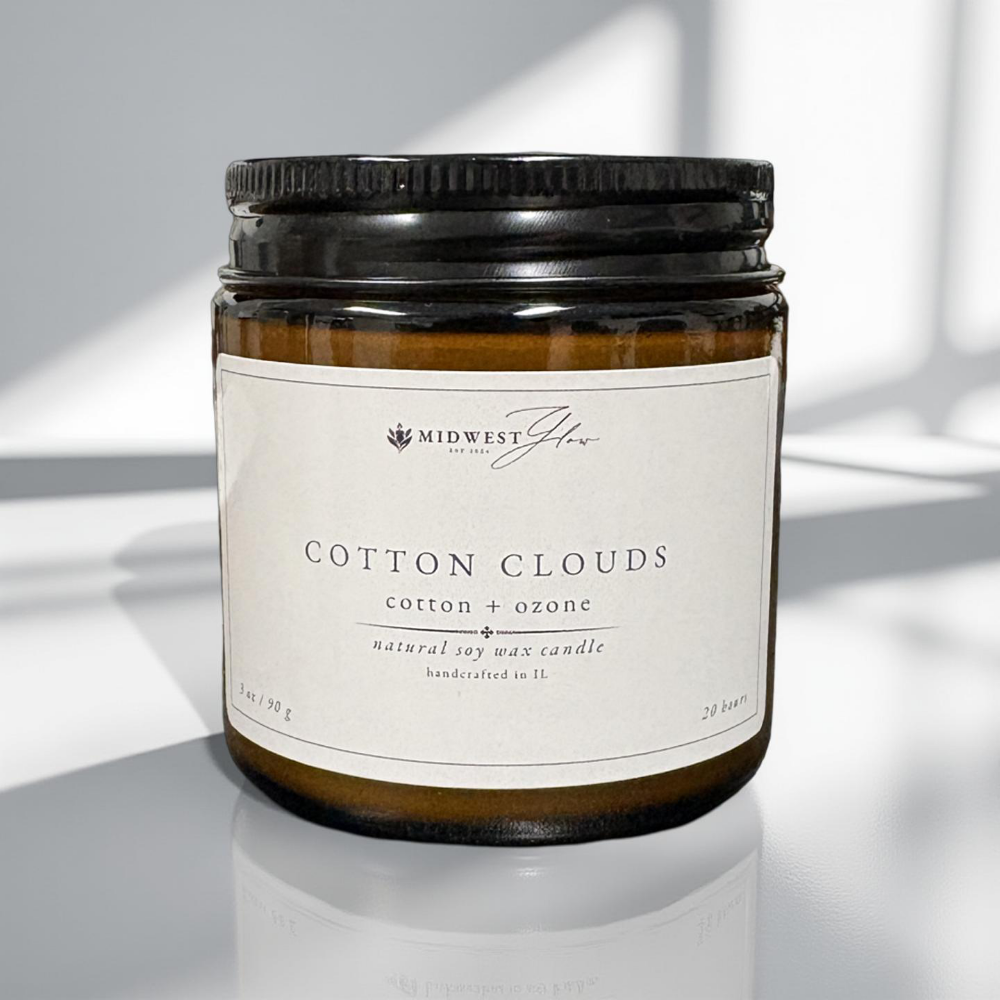 Candle jar labeled 'Cotton Clouds' with a black lid on a reflective surface.