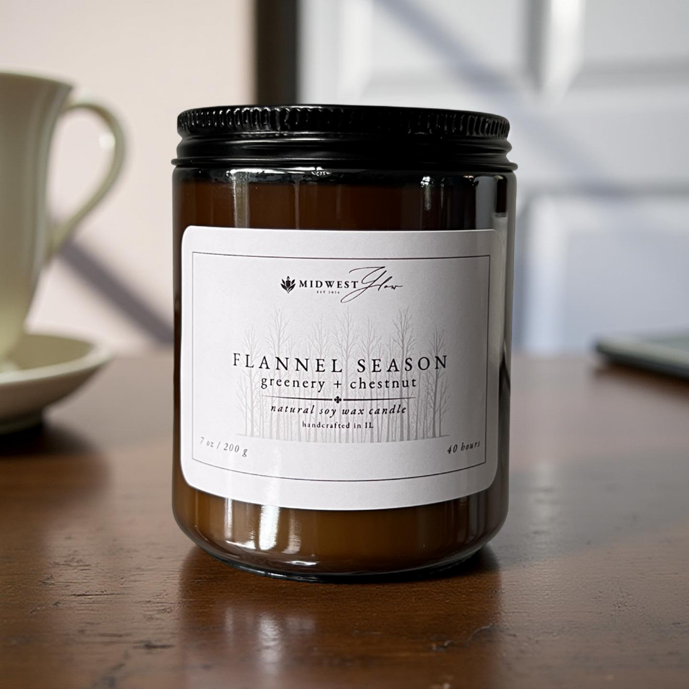 Candle jar labeled 'Flannel Season' on a wooden surface with a blurred background