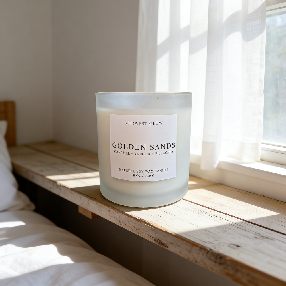 Candle labeled 'Golden Sands' on a wooden surface with a window in the background