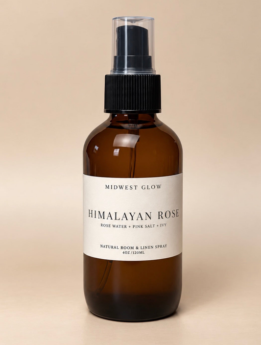 A 4oz amber glass room and linen spray bottle with a black spray nozzle and a cream label reading 'HIMALAYAN ROSE' by Midwest Glow, set against a solid beige background.