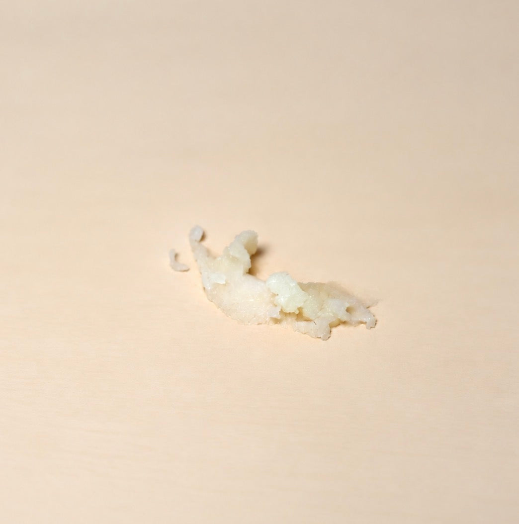 A small, irregularly shaped chunk of lip balm placed on a smooth, light beige surface.