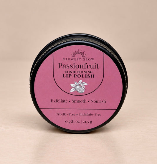 A round black tin of Midwest Glow Passionfruit Conditioning Lip Polish with a pink label, set against a solid beige background.