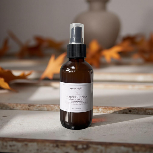 Brown spray bottle labeled 'Pumpkin Spice' on a wooden surface with autumn leaves in the background