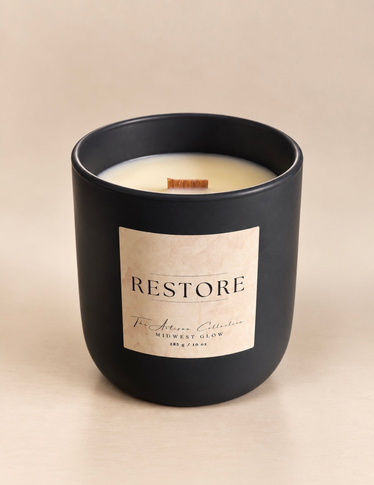 A matte black candle jar with a cream-colored wax and a light beige label that reads 'RESTORE' and 'The Aromatic Collection'.