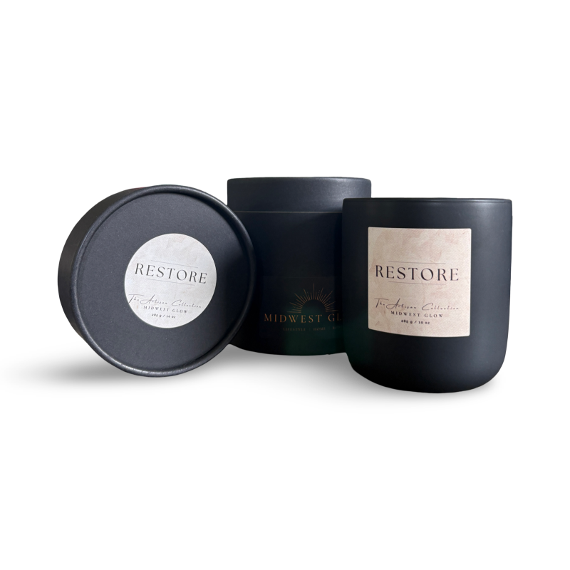 Black candle with 'Restore' label and matching black lid on a white background