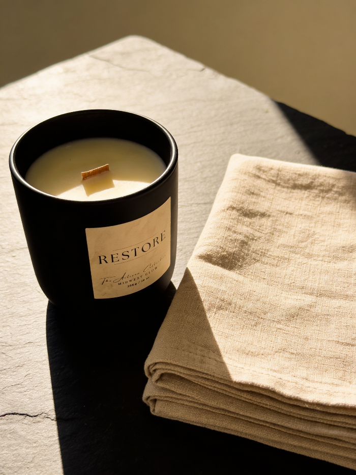 Candle labeled 'RESTORE' on a stone surface with a folded beige cloth.
