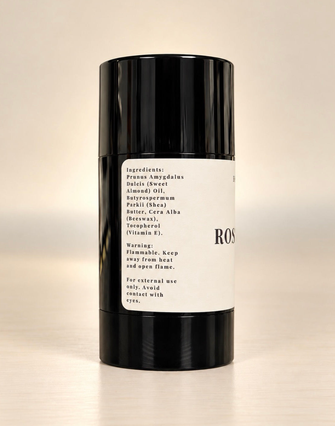 A black cylindrical deodorant stick with a white paper label, photographed against a plain light beige background.