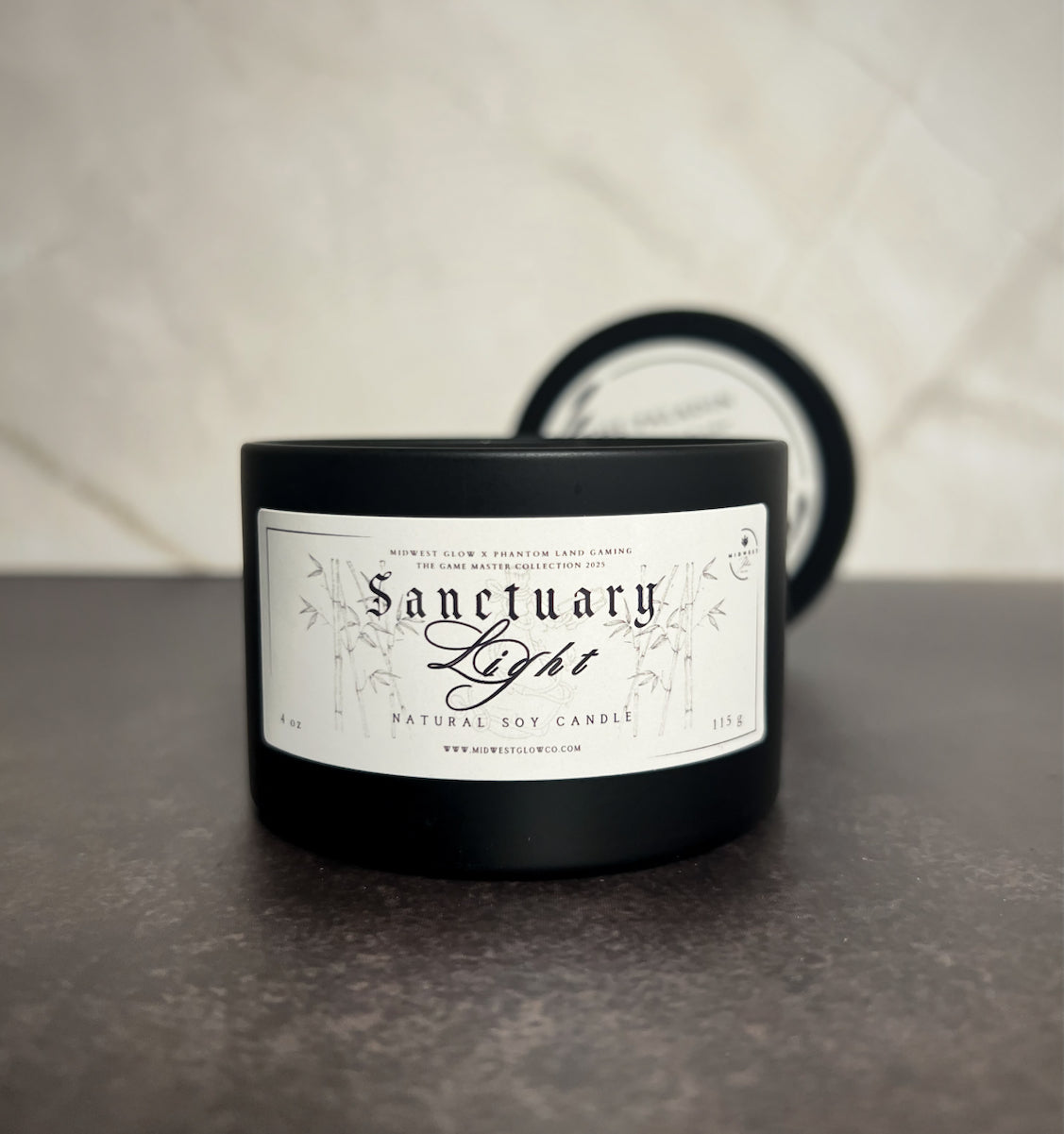 A candle in a black tin showing the label that reads Sanctuary Light by he company Midwest Glow