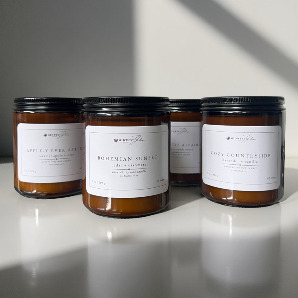 4 candles in amber glass jars sit staged against a white photo background, showcasing the Signature Collection of products offered by Midwest Glow