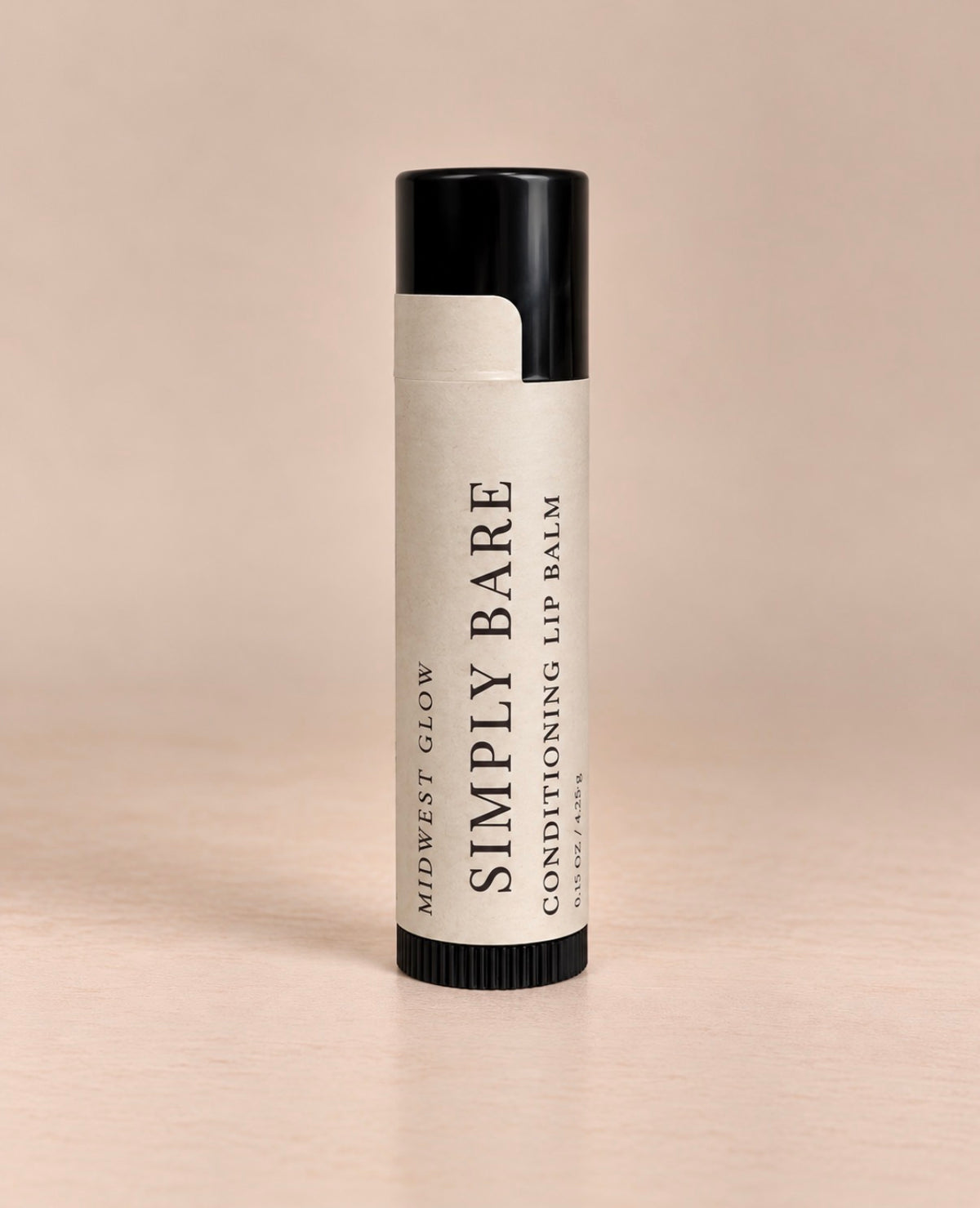 A single tube of Simply Bare Conditioning Lip Balm by Midwest Glow, standing upright on a light beige surface against a matching beige background.