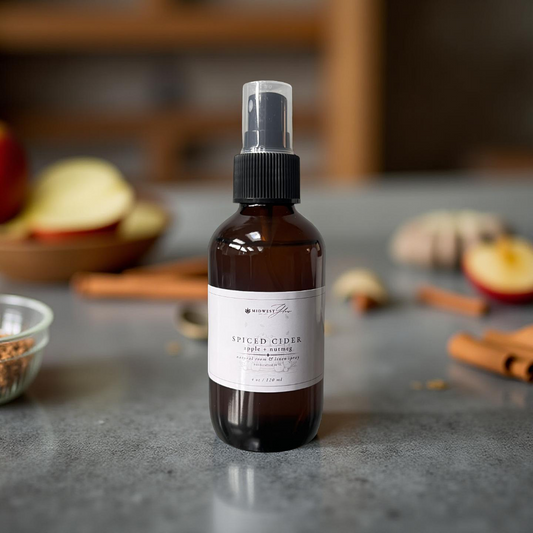 Brown spray bottle with a label on a gray surface with apples and cinnamon sticks in the background