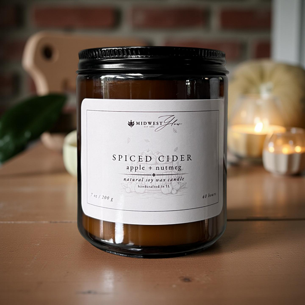 Candle labeled 'Spiced Cider' with a brick wall and blurred candle in the background
