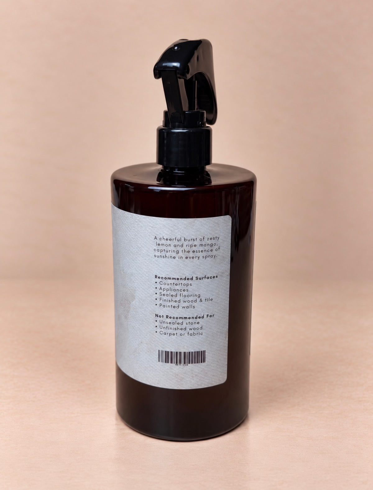 A dark amber glass spray bottle with a black trigger sprayer and a white label, photographed against a solid beige background.