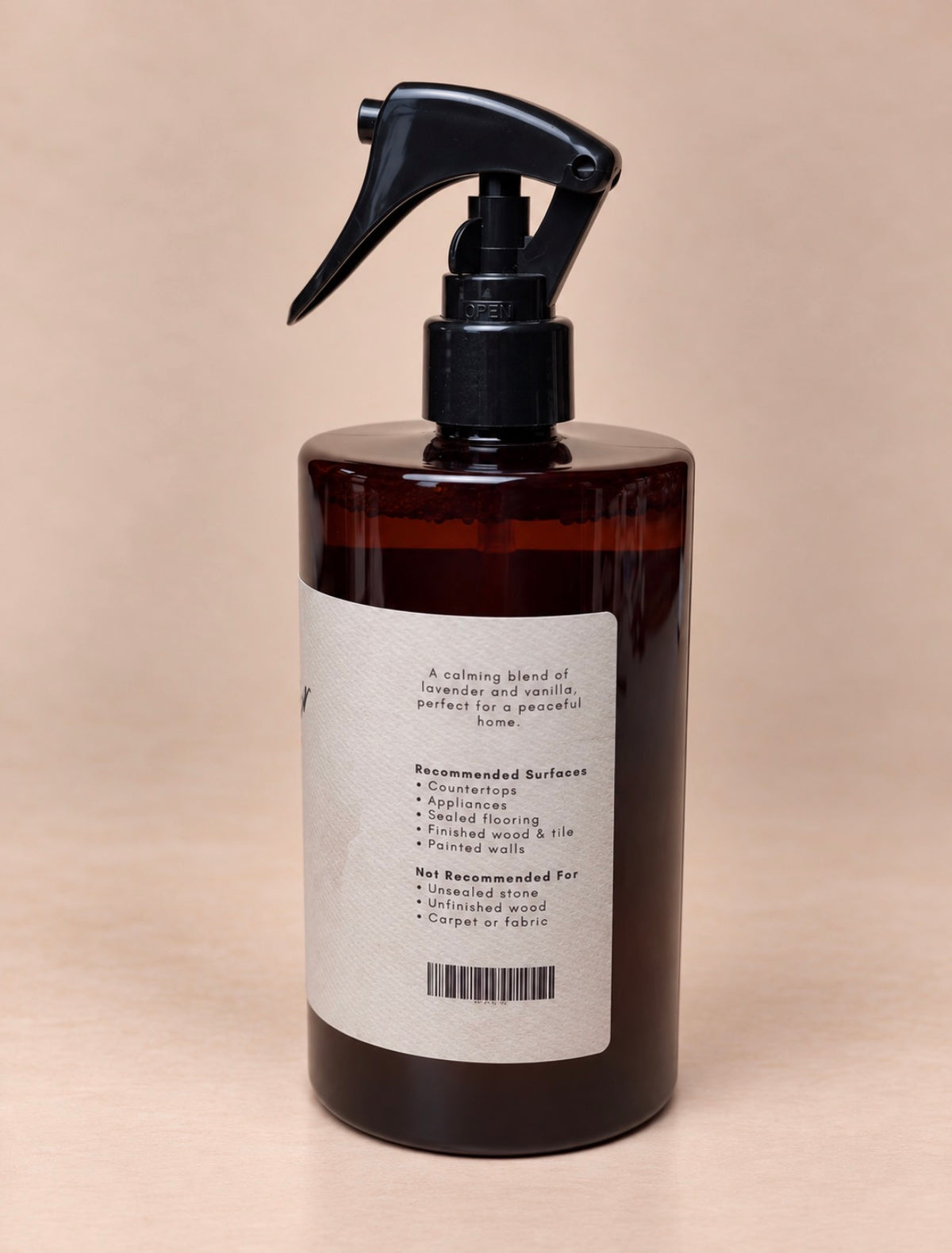 An amber glass spray bottle with a black trigger sprayer and a white paper label, photographed against a solid beige background.