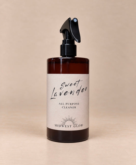 Midwest Glow Sweet Lavender All Purpose Cleaner in an amber glass spray bottle with a black spray top and a cream-colored label, set against a solid beige background.