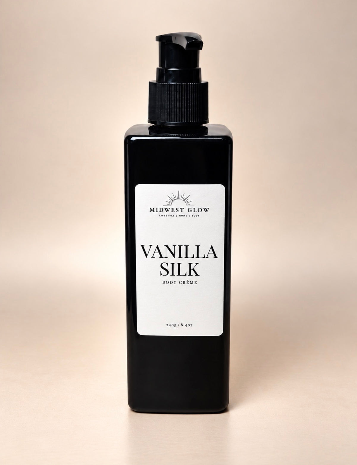 A black rectangular pump bottle of Midwest Glow Vanilla Silk Body Cream with a white label, set against a solid beige background.