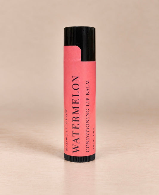 Midwest Glow Watermelon Conditioning Lip Balm in a single tube with a pink label and black cap, standing upright on a light beige surface.